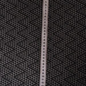 Peut inclure: Tissu noir et gris avec un motif géométrique de triangles. Un ruban à mesurer blanc est placé verticalement le long du bord droit du tissu. Le ruban mesure de 67 à 109 pouces.