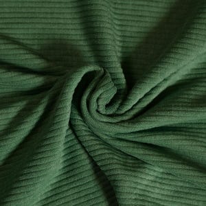 Peut inclure: Gros plan sur un tissu plié et texturé de couleur vert forêt profond. Le tissu présente un motif côtelé, les plis créant des ombres et soulignant la texture. Le matériau semble doux, potentiellement pour des vêtements ou de la décoration intérieure.