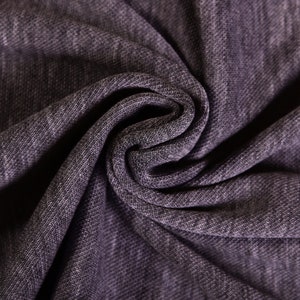 Peut inclure: Gros plan sur un tissu gris foncé avec une surface texturée et côtelée. Le tissu est plié et drapé, créant un aspect doux et fluide.