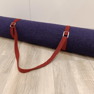 Op de afbeelding: Een donkerblauwe yogamat met een rode draagriem en zilveren gespen.