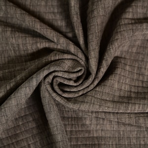 Peut inclure: Gros plan sur un tissu texturé et côtelé de couleur marron clair. Le tissu est plié et drapé, mettant en valeur le motif de côtes verticales. La matière semble douce et souple, adaptée aux vêtements ou à la décoration intérieure.