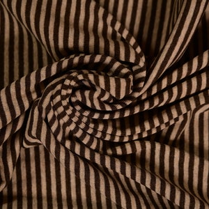 Puede incluir: Tela rayada marrón y beige con una superficie texturizada. La tela está doblada y drapeada, creando un aspecto suave y fluido.