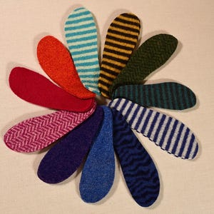 Op de afbeelding: Een set van tien viltstofstalen in verschillende kleuren en patronen, waaronder blauw, groen, rood, roze en geel. De stalen zijn in een cirkel gerangschikt.