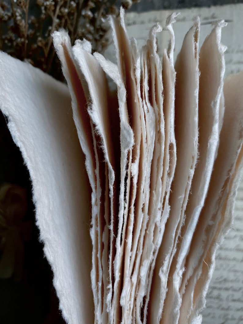 Puede incluir: Una pila de hojas de papel hechas a mano con bordes &aacute;speros e irregulares. El papel es de color blanco crema y tiene una superficie texturizada.