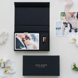 May include: A black rectangular presentation box with a magnetic lid, featuring the gold text LANA MARIE PHOTOGRAPHER. The open box contains a printed photograph of a couple and a small gold rectangular USB drive in a dedicated compartment.