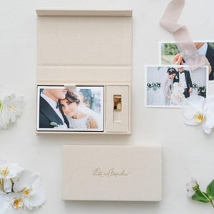May include: A beige rectangular keepsake box with a hinged lid, featuring the embossed text Peter and Veronika. The open box contains a printed photograph of a couple and a gold USB drive. Two additional wedding photographs are placed nearby.