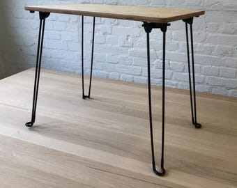 May include: A small, rectangular wooden table with a light brown finish. The table has four black hairpin legs. The table is approximately 30 inches long and 15 inches wide.