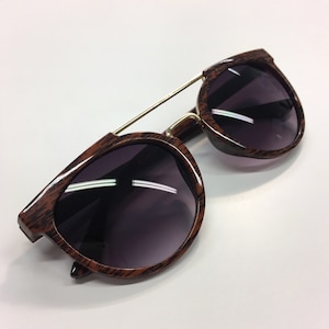May include: Brown wood-grain sunglasses with dark lenses and a gold metal frame.