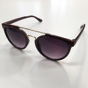 May include: Brown wood-grain framed sunglasses with a gold metal bridge and dark tinted lenses.