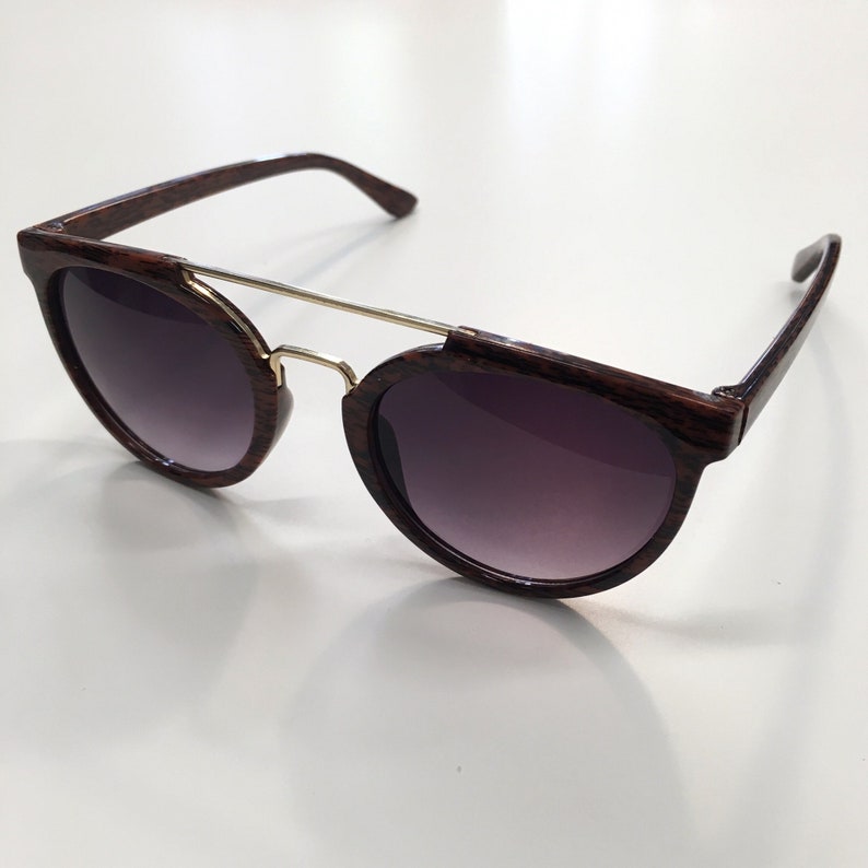 May include: Brown wood-grain framed sunglasses with a gold metal bridge and dark tinted lenses.
