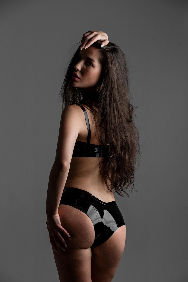 May include: A black latex two-piece set consisting of a bra top with thin shoulder straps and matching high-cut briefs. The material has a high-gloss, reflective finish that catches the light, creating a smooth and sleek appearance throughout.