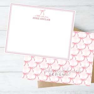 May include: A white card with a pink border and a pink bow at the top. The text "a little note from ANNIE SINCLAIR" is printed on the card. The card is sitting on top of a pink and white gingham pattern.