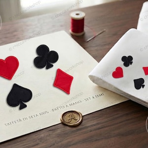 May include: A set of four embroidered playing card suit patches featuring a red heart, a black club, a black spade, and a red diamond. The patches are displayed on a cream card with the text TAFFETÀ DI SETA 100% - FATTO A MANO - SET 4 SEMI.