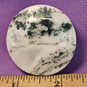 May include: A round, white agate stone with green moss inclusions. The stone is approximately 2 inches in diameter.