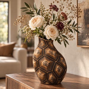 Könnte beinhalten: Eine dekorative Vase mit einem dunkelbraunen und goldenen Sechseckmuster, das an einen Schildkrötenpanzer erinnert, gefüllt mit einem Blumenarrangement aus weißen Gartenrosen, kleinen weißen Blüten, dunkelroten Blumen und grünen Blättern.