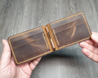 May include: A brown leather wallet with a money clip and multiple card slots. The wallet has yellow stitching around the edges.