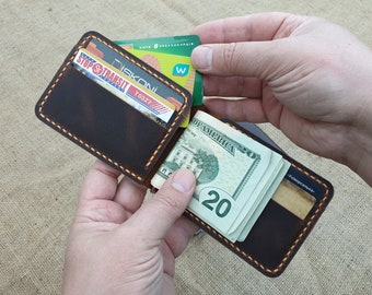 May include: A brown leather wallet with a money clip and multiple card slots. The wallet is open and has cash and cards inside.