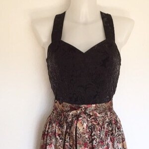 May include: A vintage-style dress displayed on a mannequin. The bodice is black with a textured pattern, and the skirt features a floral print in shades of brown, red, and cream. The dress has a halter neckline and a full, flowing skirt.