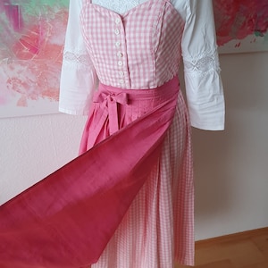 May include: A pink and white gingham dirndl with a pink sash and a white blouse with lace trim.