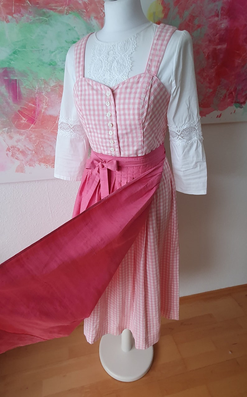 May include: A pink and white gingham dirndl with a pink sash and a white blouse with lace trim.