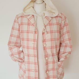 Könnte beinhalten: Cremefarbene Jacke mit rotem Karomuster und Kapuze. Die Jacke hat eine Knopfleiste, zwei Taschen und wird auf einer Schaufensterpuppe präsentiert. Die Kapuze und die Innenschicht sind einfarbig cremefarben.