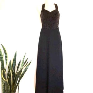 May include: A black formal gown with a sweetheart neckline and wide straps. The bodice features a textured, dark brown pattern, while the skirt is a solid, flowing black fabric. The dress is displayed on a mannequin against a white background.