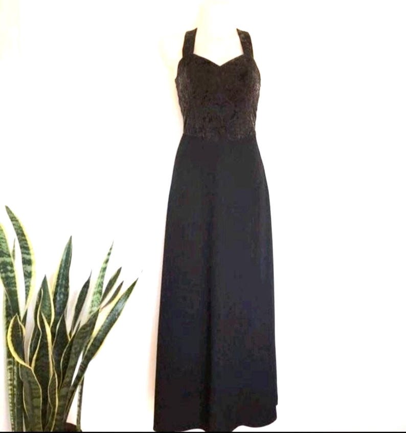 May include: A black formal gown with a sweetheart neckline and wide straps. The bodice features a textured, dark brown pattern, while the skirt is a solid, flowing black fabric. The dress is displayed on a mannequin against a white background.