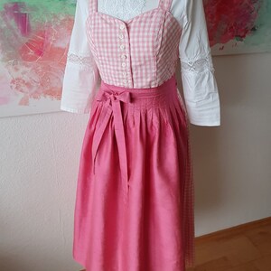 May include: A pink and white gingham dirndl with a pink satin skirt and a white blouse with lace trim.