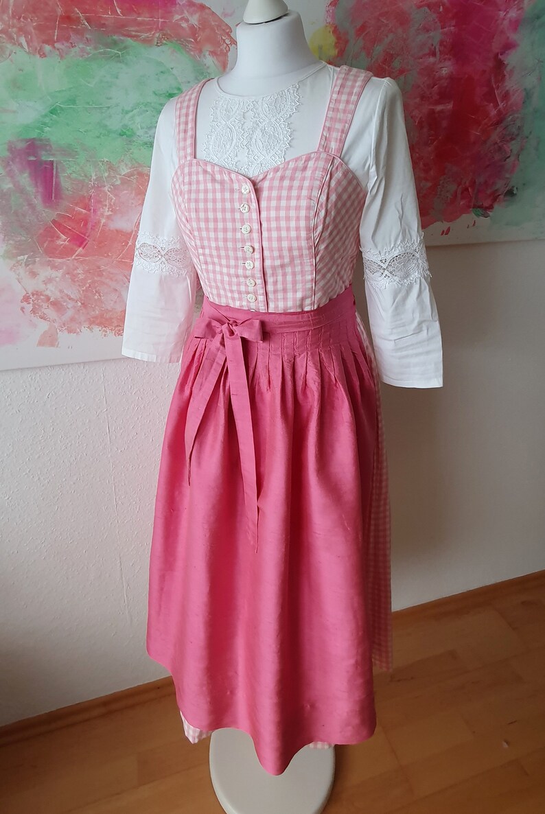 May include: A pink and white gingham dirndl with a pink satin skirt and a white blouse with lace trim.
