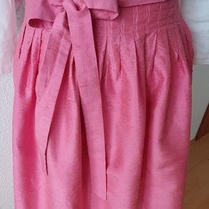 May include: A pink silk skirt with pleats and a matching bow tie. The skirt is tied at the waist and has a simple design.
