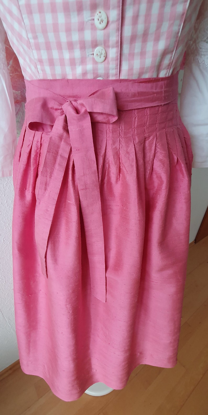 May include: A pink silk skirt with pleats and a matching bow tie. The skirt is tied at the waist and has a simple design.
