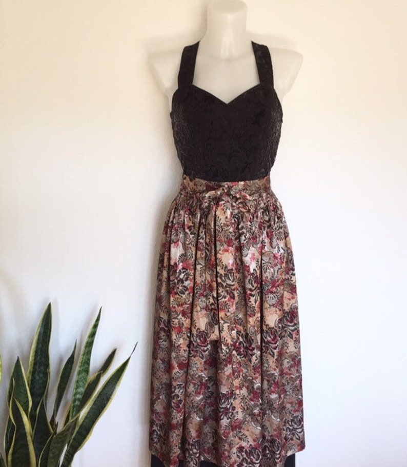 May include: A vintage-style dress displayed on a mannequin. The bodice is black with a textured pattern, and the skirt features a floral print in shades of brown, red, and cream. The dress has a halter neckline and a full, flowing skirt.