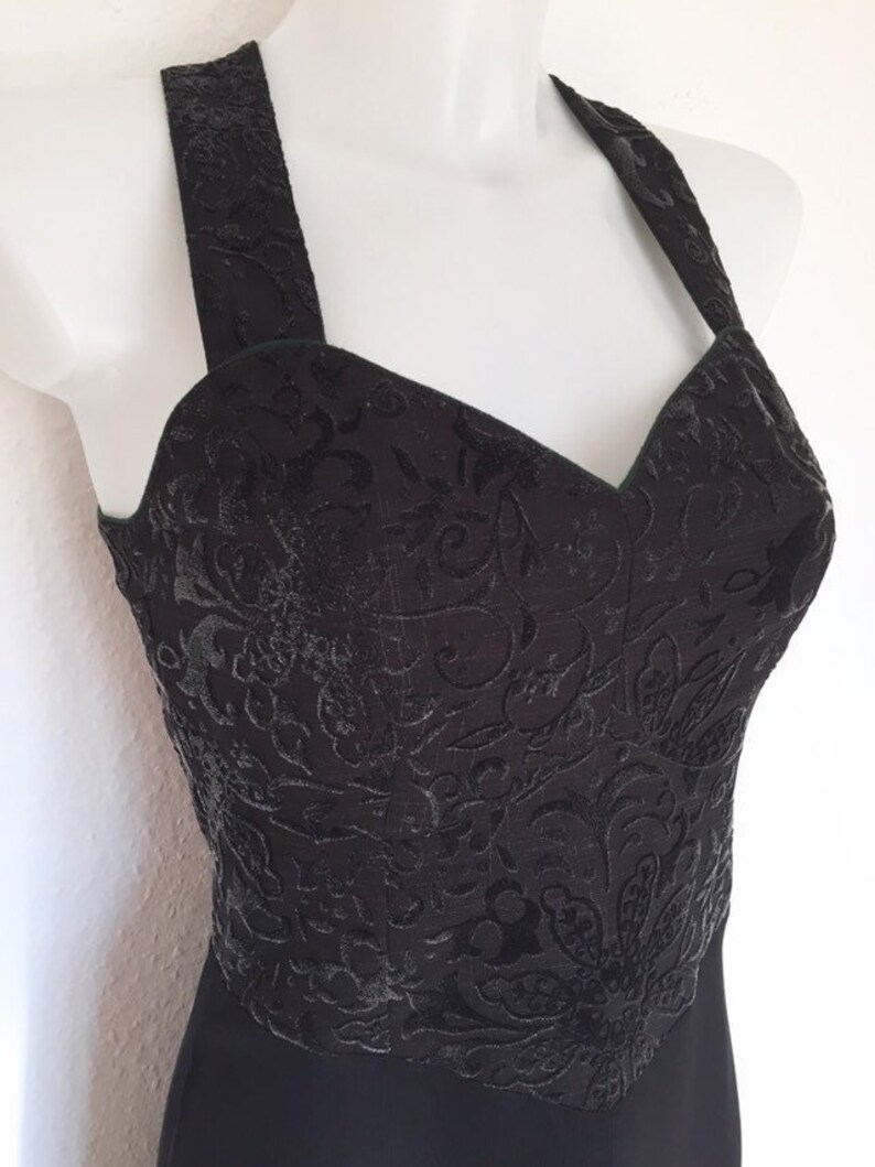 May include: Black halter top dress with a textured floral pattern on the bodice. The dress features a sweetheart neckline and wide straps. The lower portion of the dress is a solid black color.