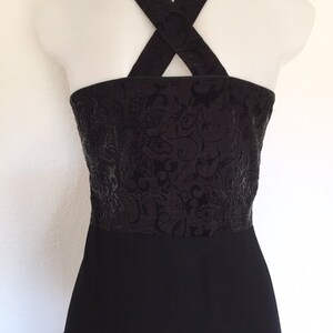 May include: Black dress with a textured bodice featuring a floral pattern. The dress has a halter-style neckline with crisscross straps in the back. The lower portion of the dress is a solid black color.