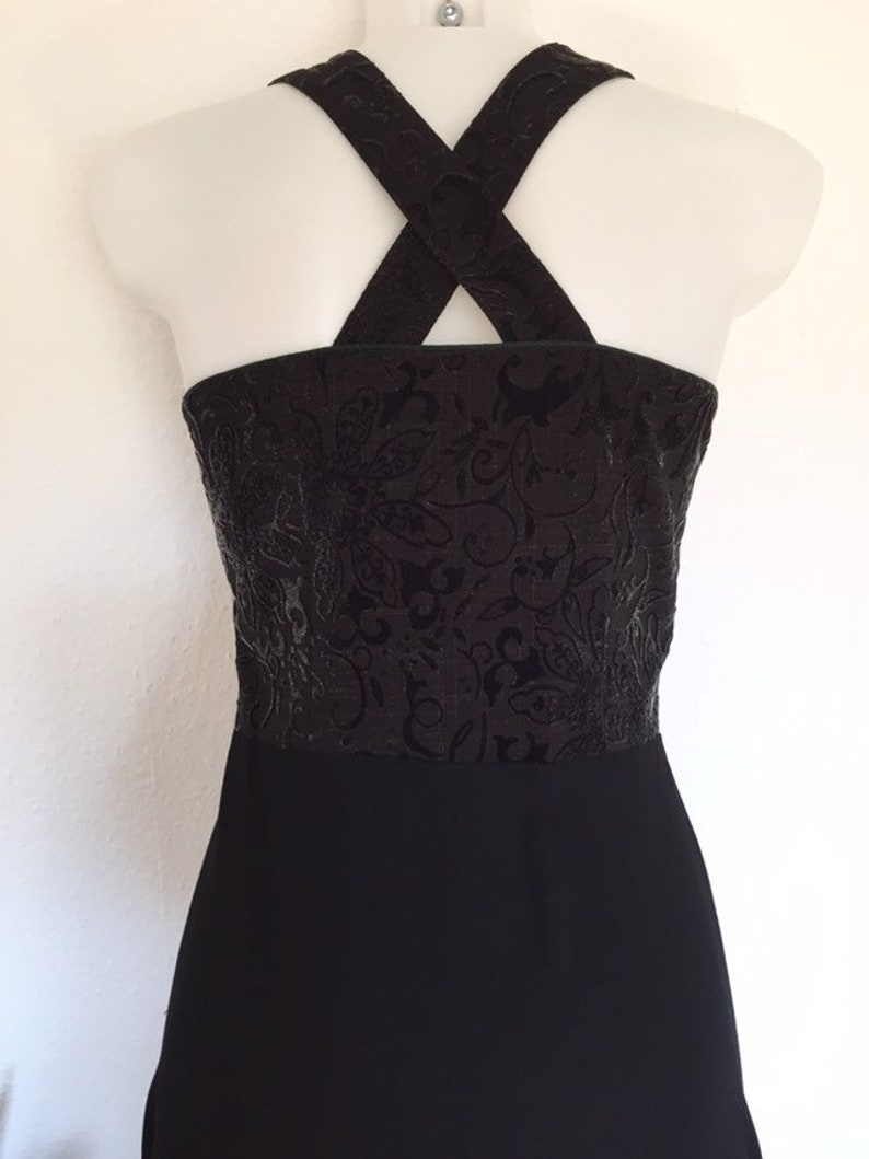 May include: Black dress with a textured bodice featuring a floral pattern. The dress has a halter-style neckline with crisscross straps in the back. The lower portion of the dress is a solid black color.