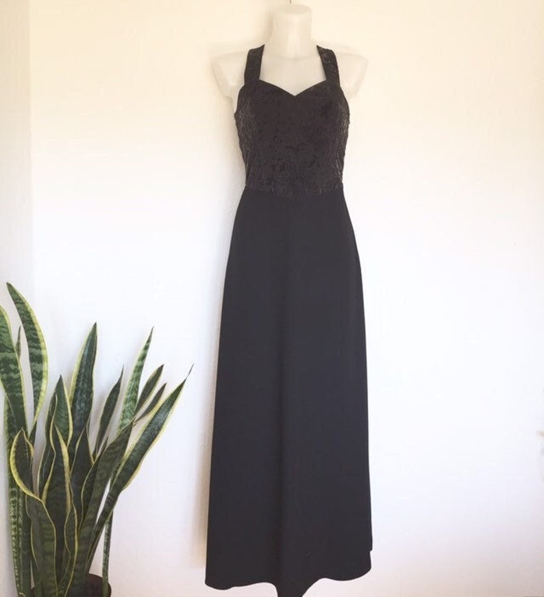 May include: A black halter-style evening gown displayed on a mannequin. The bodice features a textured, dark pattern, while the skirt is a solid, flowing black. The dress is floor-length, suitable for formal events.