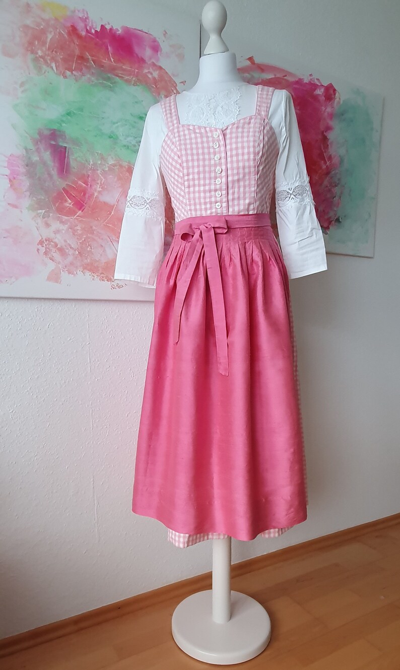 May include: A pink dirndl with a white and pink gingham bodice and a white blouse with lace trim.