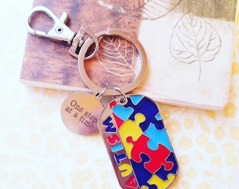 May include: Silver keychain with a puzzle piece design in red, blue, and yellow, with the word "AUTISM" in blue. A smaller round charm reads "One step at a time."
