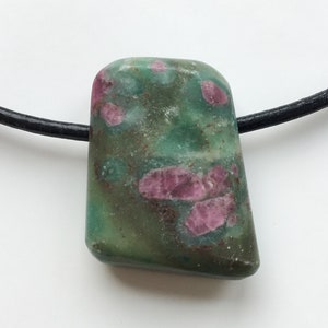 Könnte beinhalten: Ein grüner und rosa Steinanhänger an einer schwarzen Kordelkette. Der Stein hat eine Mischung aus grünen und rosa Farbtönen mit einer glatten, polierten Oberfläche. Die Halskette ist schlicht und elegant, für den Alltag geeignet.