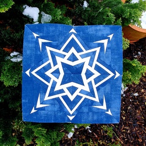 Könnte beinhalten: Ein blauer und weißer geometrischer Quiltblock mit einem Sternmuster. Der Stern besteht aus weißen Dreiecken und Quadraten auf blauem Hintergrund.