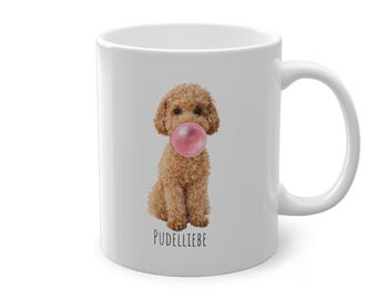 May include: White ceramic mug featuring a brown poodle with a pink bubble gum bubble. The word "PUDDELLIEBE" is printed in black below the dog. The mug has a curved handle.