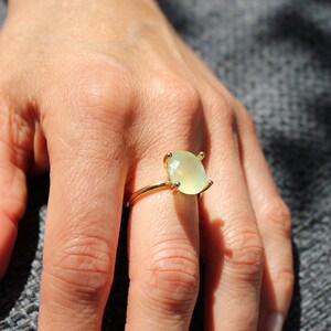 Könnte beinhalten: Ein goldener Ring mit einem hellgrünen ovalen Edelstein, der in einer Krappenfassung sitzt.