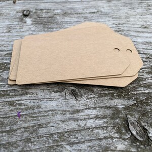 Pode incluir: Um conjunto de tr&ecirc;s etiquetas de presente de papel castanho com dois furos perfurados no topo.