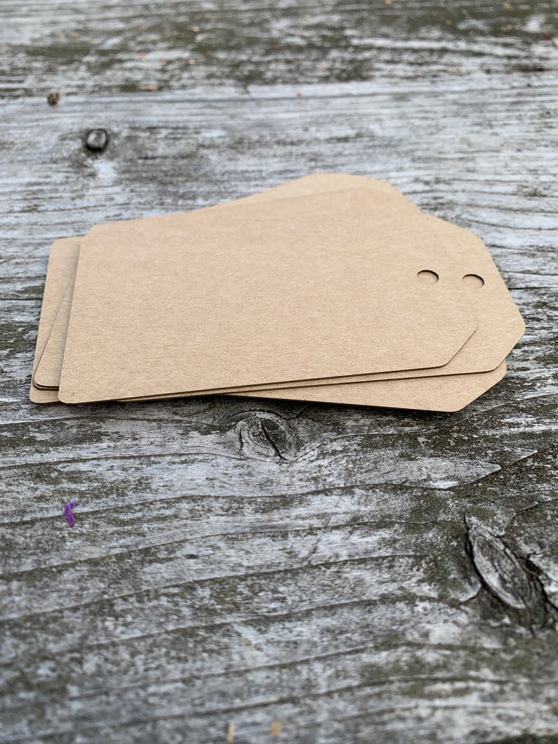 Pode incluir: Um conjunto de tr&ecirc;s etiquetas de presente de papel castanho com dois furos perfurados no topo.