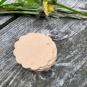 May include: A stack of brown, scalloped-edge gift tags with a hole punched in the top. The tags are on a wooden surface.