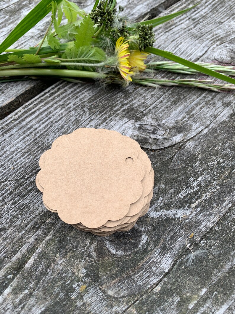 May include: A stack of brown, scalloped-edge gift tags with a hole punched in the top. The tags are on a wooden surface.