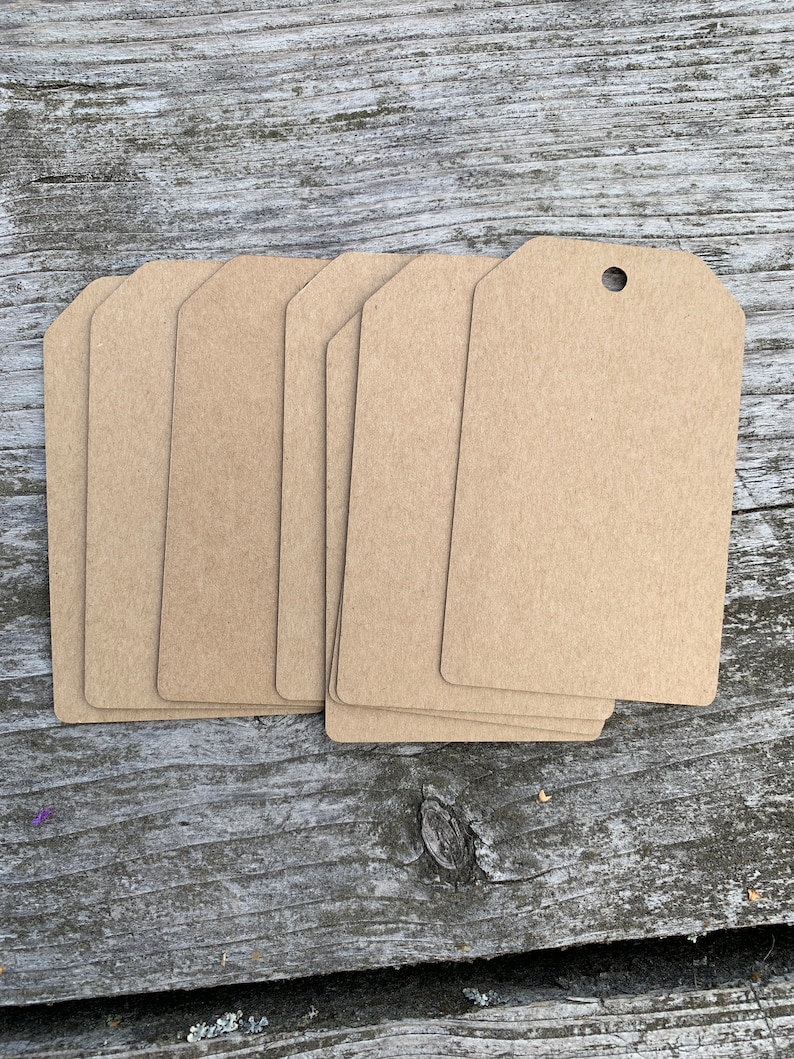 Pode incluir: Um conjunto de oito etiquetas de presente de papel kraft castanho com um furo perfurado no topo. As etiquetas est&atilde;o em branco e prontas para serem escritas.