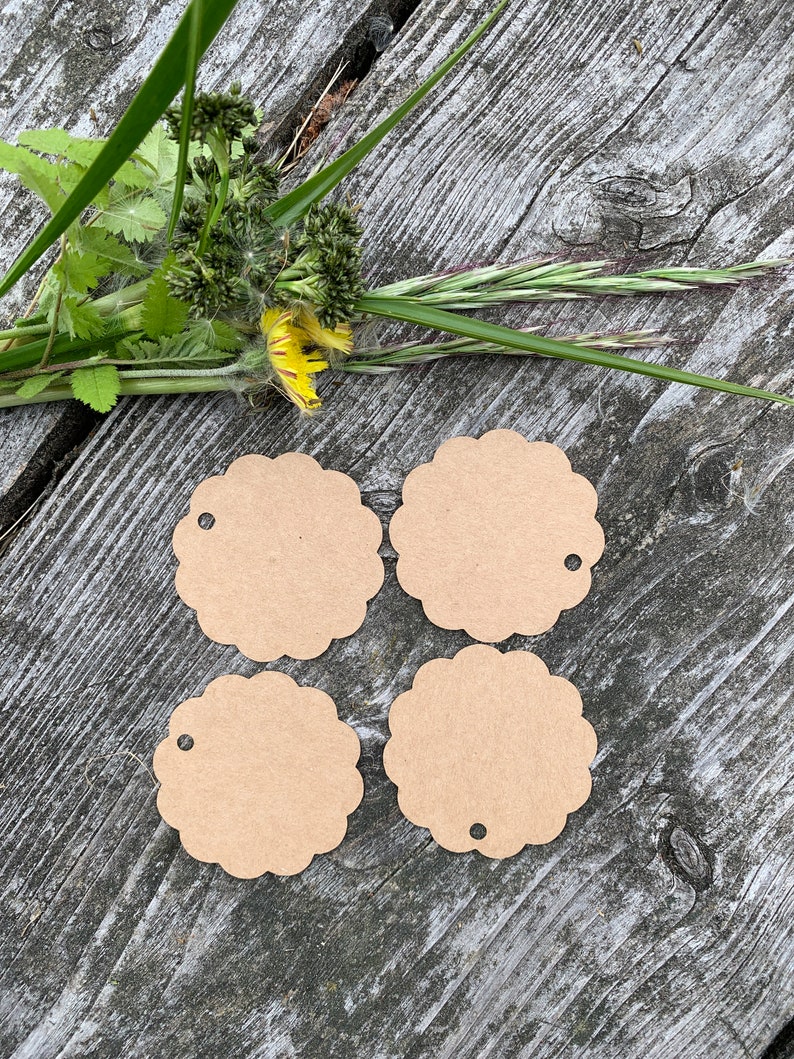 May include: Four brown scalloped circle gift tags with a hole punched in the top. The tags are on a wooden surface.