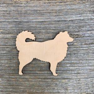 Pode incluir: Um recorte de madeira de uma silhueta de cão. O cão está em pé com o rabo enroscado. O recorte é de cor castanho claro e tem uma superfície lisa.