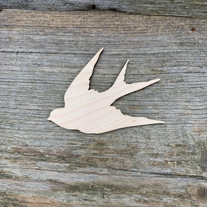 Puede incluir: Un recorte de madera de un pájaro en vuelo. El pájaro está hecho de madera marrón claro y tiene un diseño simple y elegante.